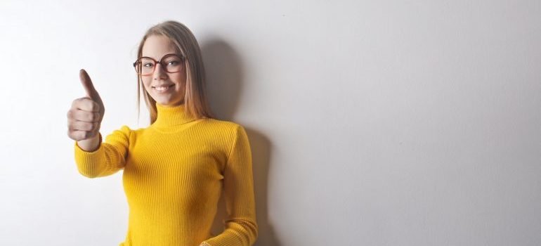 A smiling woman in yellow sweater holding thumbs up.