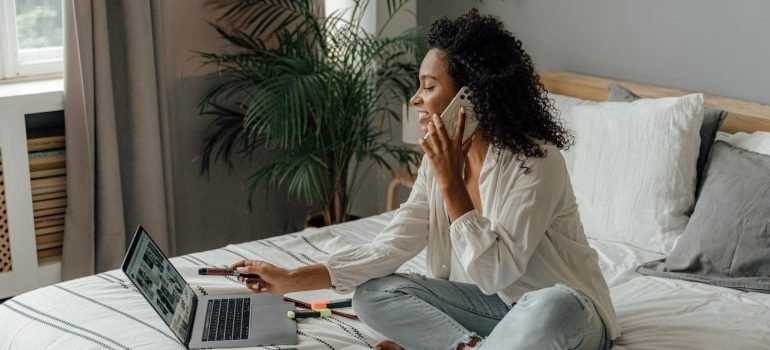 A woman using a phone and laptop to find the best storage units Queens NY can offer.