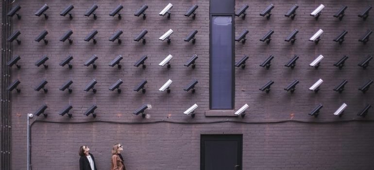 Two people standing under an excessive number of CCTV cameras.