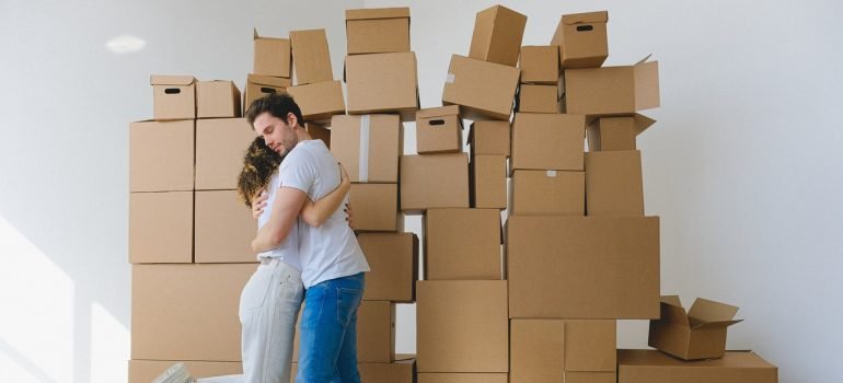A young couple hugging in front of the pile of cardboard boxes.