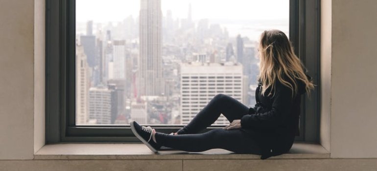 a girl sitting by the window and thinking about reasons why New Yorkers move