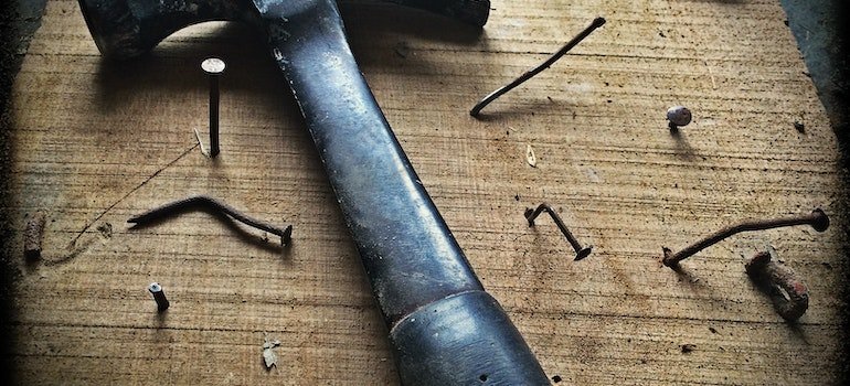 Black hammer on a brown wooden table with nails scattered