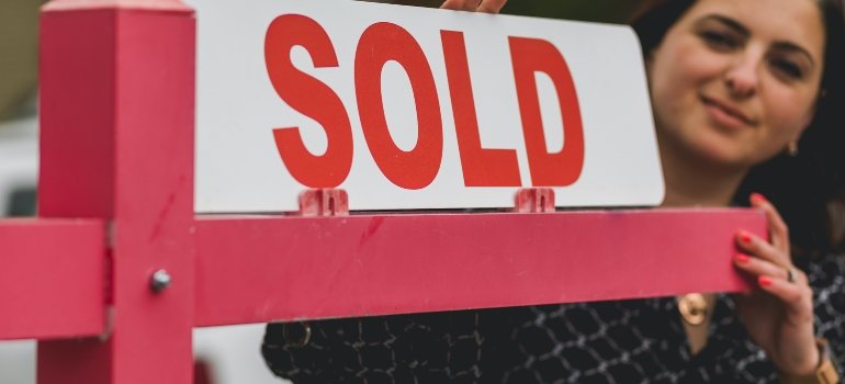A real estate agent who can help you understand the cost of temporary housing in NYC, standing next to the "Sold" sign
