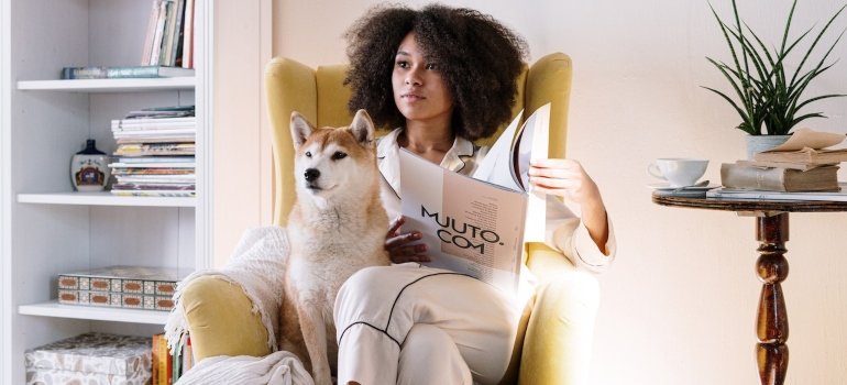 A woman sitting and reading a book with her dog.