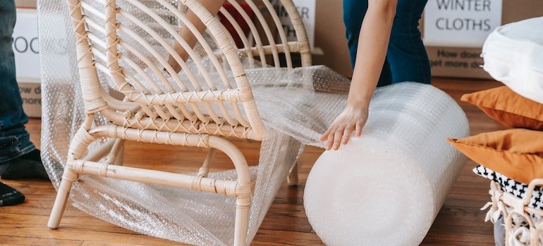 Person wrapping a chair to protect wooden furniture from damage in storage.