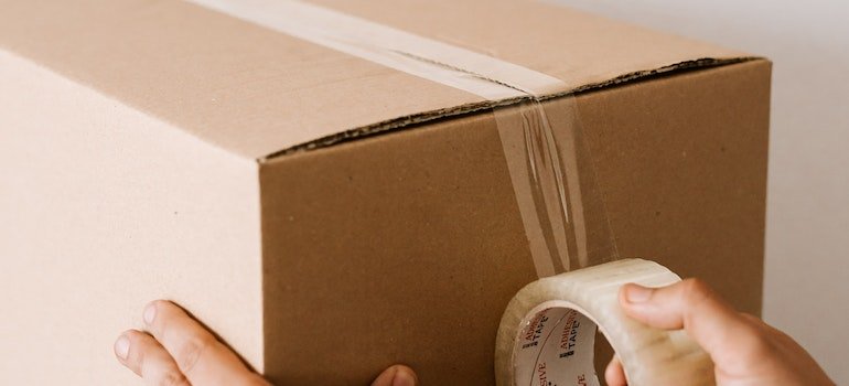 A person putting tape on a box to close it, as downsizing your Manhattan apartment is best done by getting a storage unit.