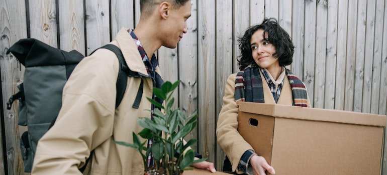 A man and a woman looking at each other while carrying boxes.