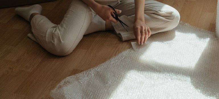a person sitting on the floor and preparing to cut bubble wrap