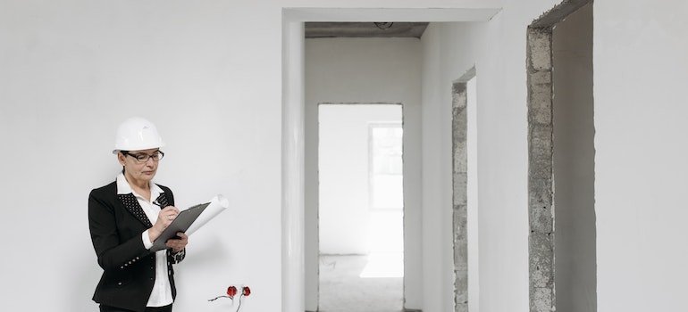 Woman in a black suit stands next to a white wall