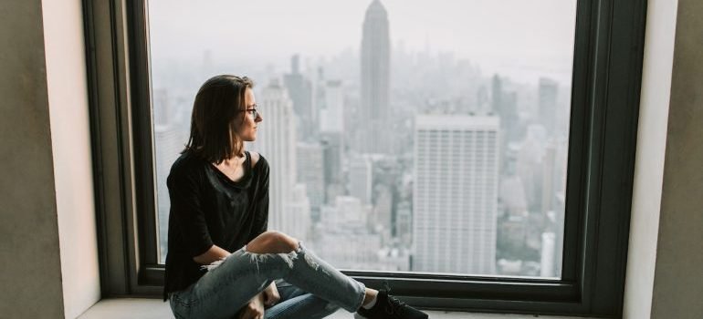 A girl sitting by a window with the view of New York city