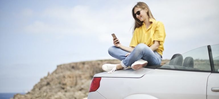 A girl sitting on a car browsing what is better - Climate-Controlled vs Outdoor Vehicle Storage