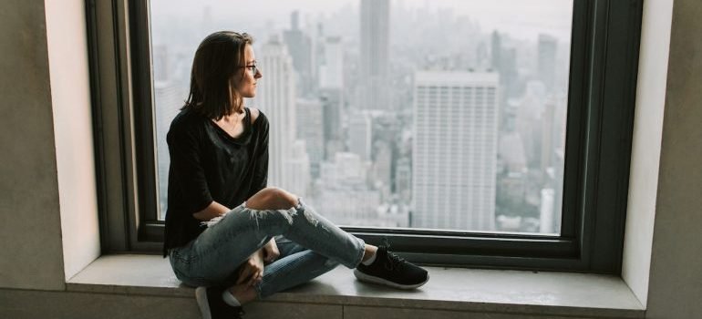 A girl in front of the window in NYC thinking how to keep your NYC apartment organized and clutter-free