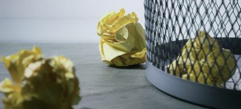 A trash bin with papers around it