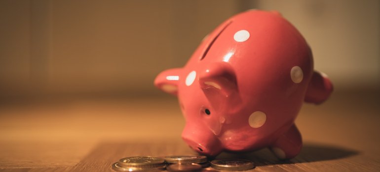 A pink piggy bank leaning on coins.