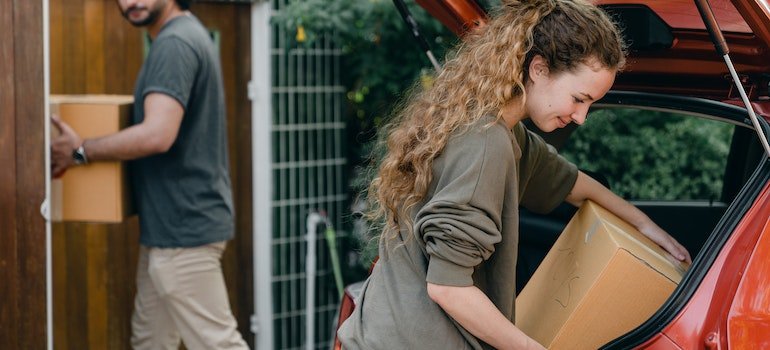 A young couple putting boxes into a car trunk.