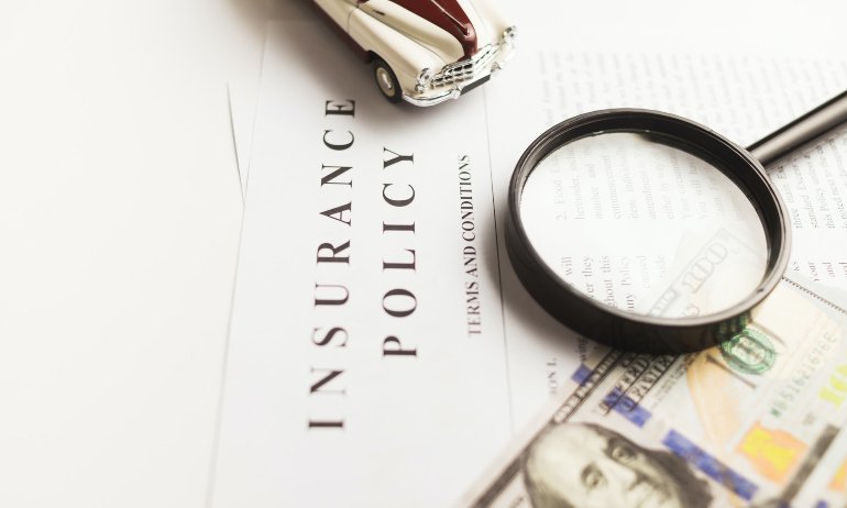 An insurance policy with a magnifying glass, a model of a car, and a dollar bill on it.