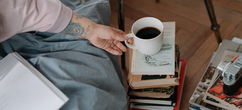 A person placing a cup of coffee onto a pile of books.