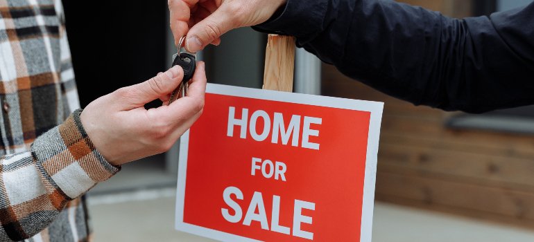 one person handing the keys to another in front of a sign that says "home for sale"