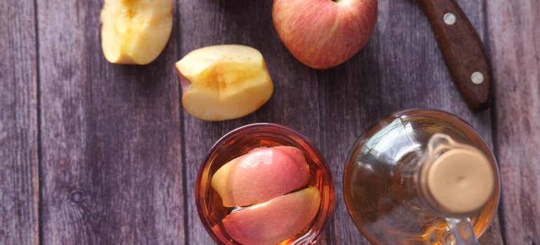A glass of apple cider with slices of apple in it and a bottle next to it.