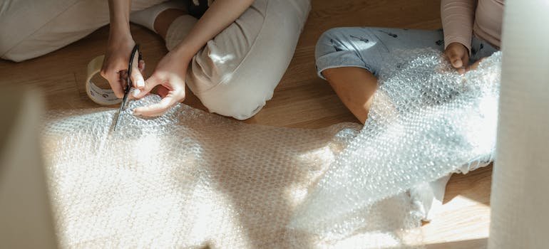 People cutting bubble wrap they will use to store antique lamps securely