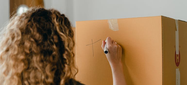 A woman labeling a cardboard moving box.