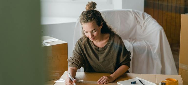 A woman writing something on a cardboard box.