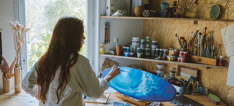 A woman painting and using a storage unit for that because she knows storage units can expand your apartment.