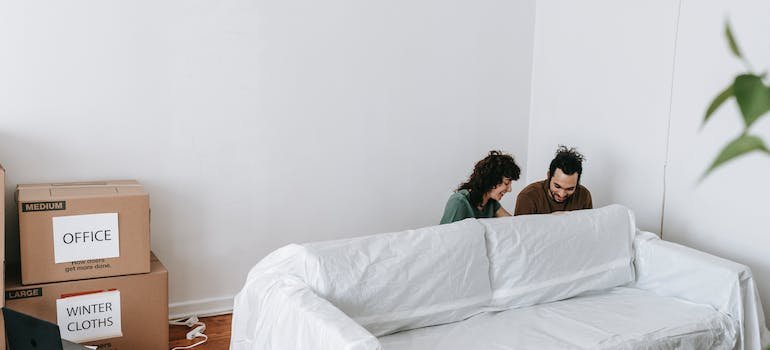 A couple wrapping a couch with white linen