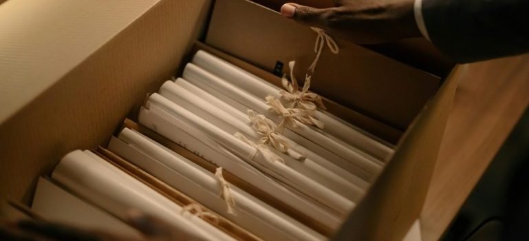 Documents in a cardboard box, hands holding sides of the box