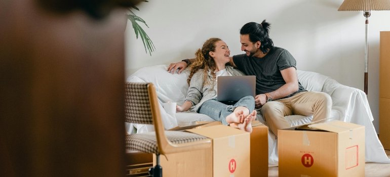 A couple sitting on a sofa and surrounded with moving boxes after moving from Wakefield to Castle Hill.