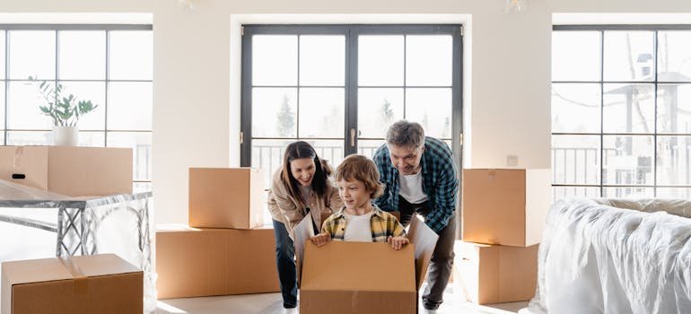 A couple looking at their son playing in a moving cardboard box.