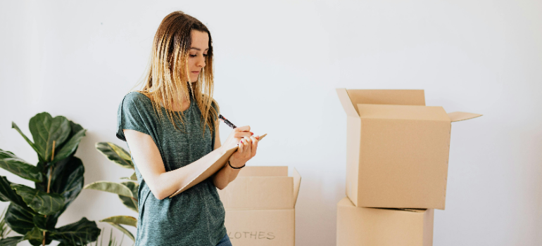 A woman surrounded with cardboard boxes making a list.