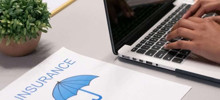 The word insurance written on a piece of paper and a person working on a laptop.