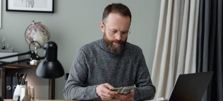 A man sitting at a desk and counting the money he saved thanks to renting a shared storage unit.