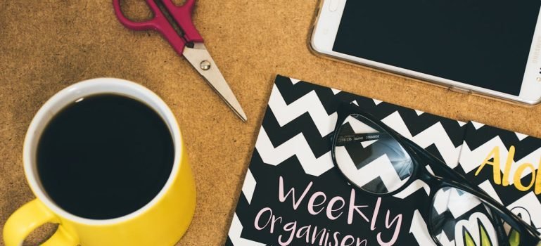 A cup of coffee, a tablet, and a planner on the desk.