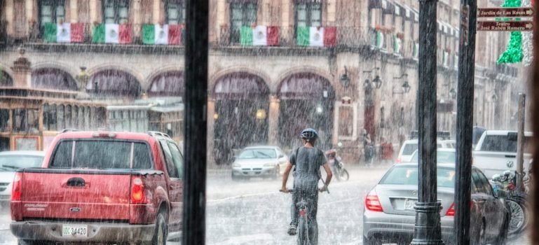 Parked cars and a man on a bike on the rain.