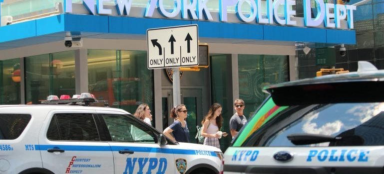 People and police cars in front of NYPD.