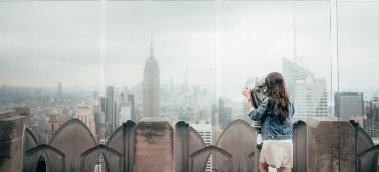 A woman in blue denim jacket standing on top of a building and ooking at NYC cityscape.