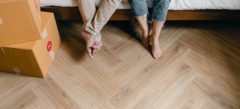 A couple sitting on a bed barefoot and beginning to pack for a move.