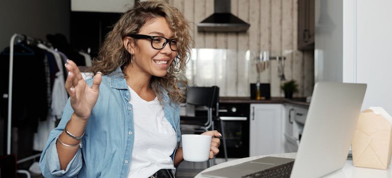 A woman waving and smiling in front of a laptop.