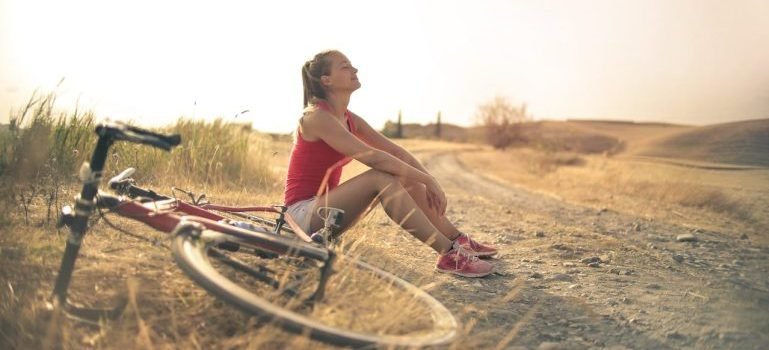 A woman sitting on the ground and a bike near her.