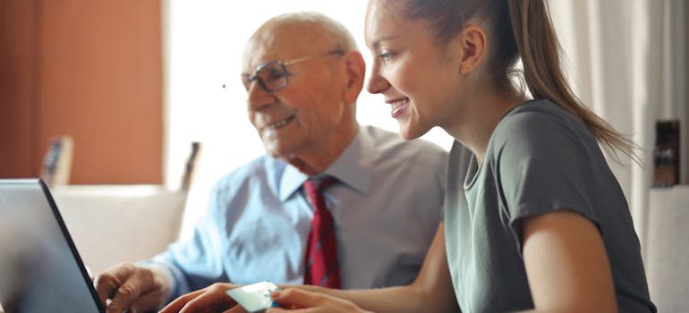 A senior man and a young woman reading on a laptop.