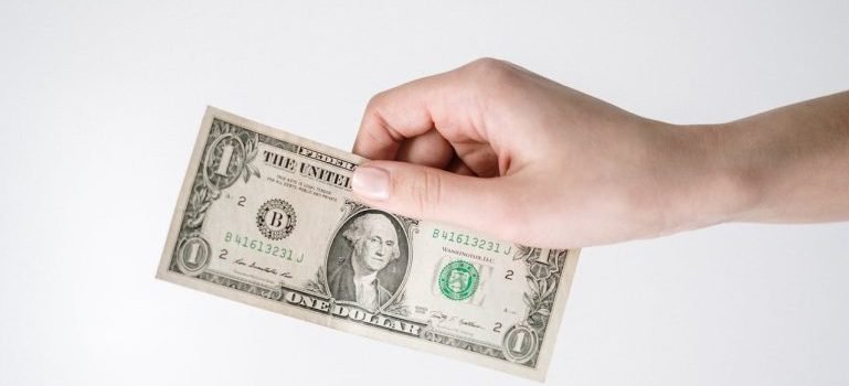 A hand holding a dollar bill to save for living in Long Island City
