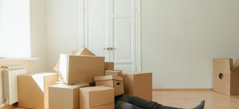 A man on the floor under a pile of cardboard boxes while preparing himself to pack and store camping gear