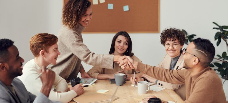 Two co workers shaking hands at a staff meeting.