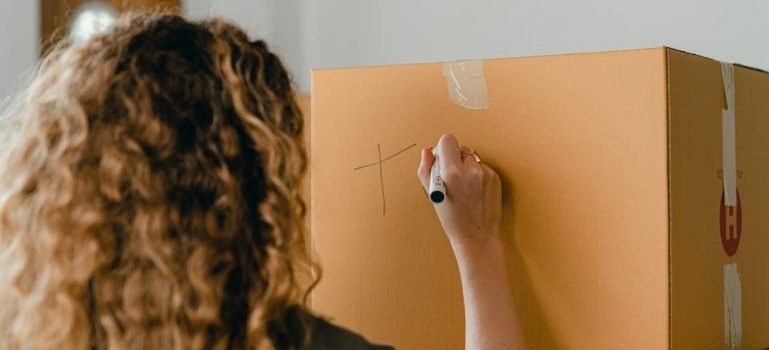 A woman labeling a cardboard box.