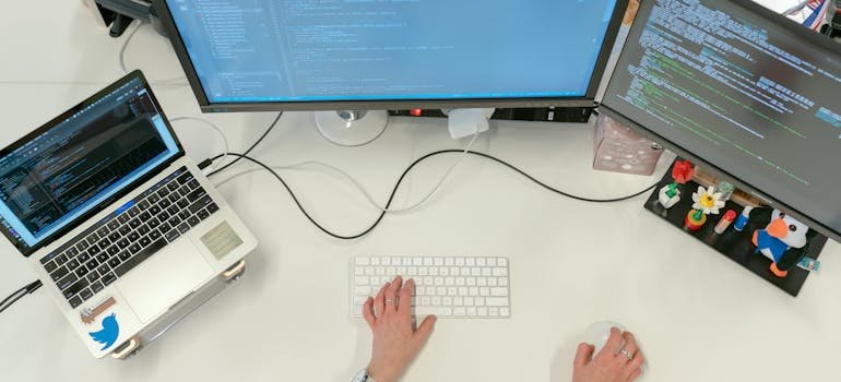 A person typing on a laptop in front of three monitors