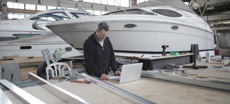 A man surrounded with boats reading on a laptop about storing your boat over the off-season