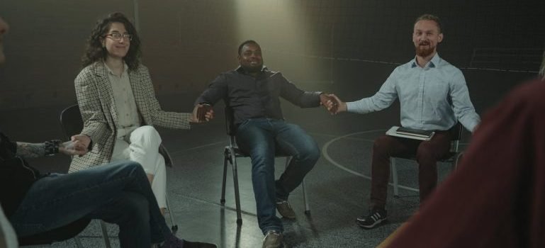 People sitting and holding hands in a dark room while trying to build social connections after moving to the Bronx.