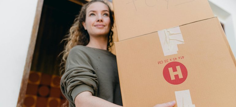 A woman carrying a cardboard box while preparing items for long-term storage.